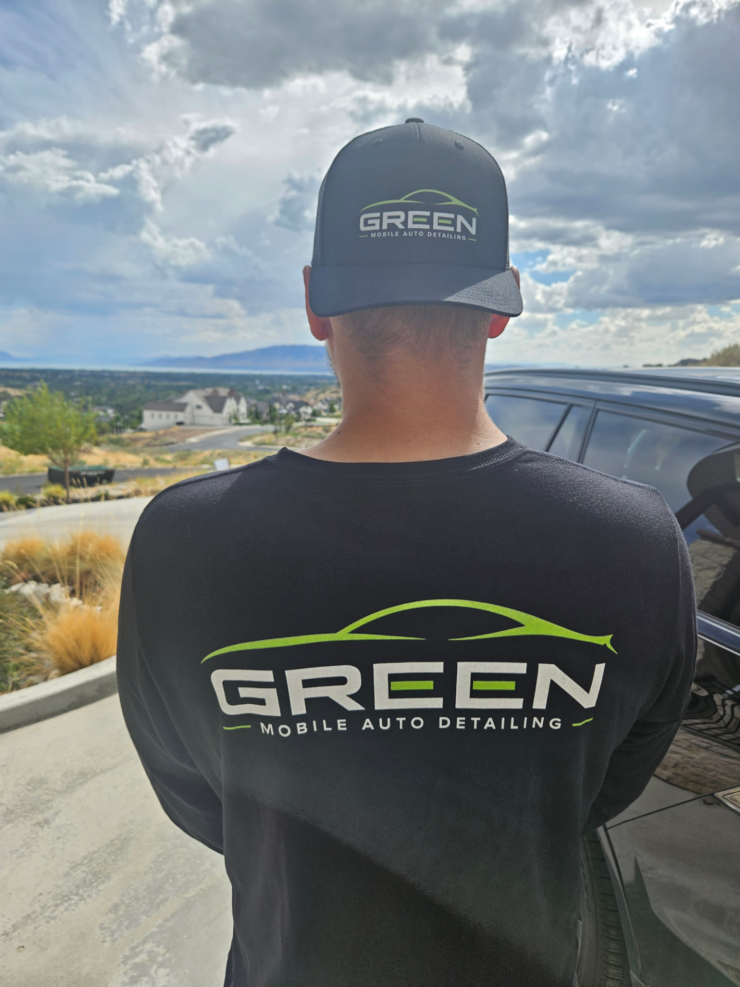 Conner in Green Mobile Auto Detailing branded gear looking out over the Utah County valley beside a client vehicle